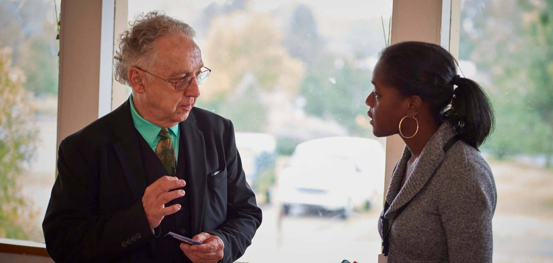 Two people in professional attire having a conversation in front of a bright window.