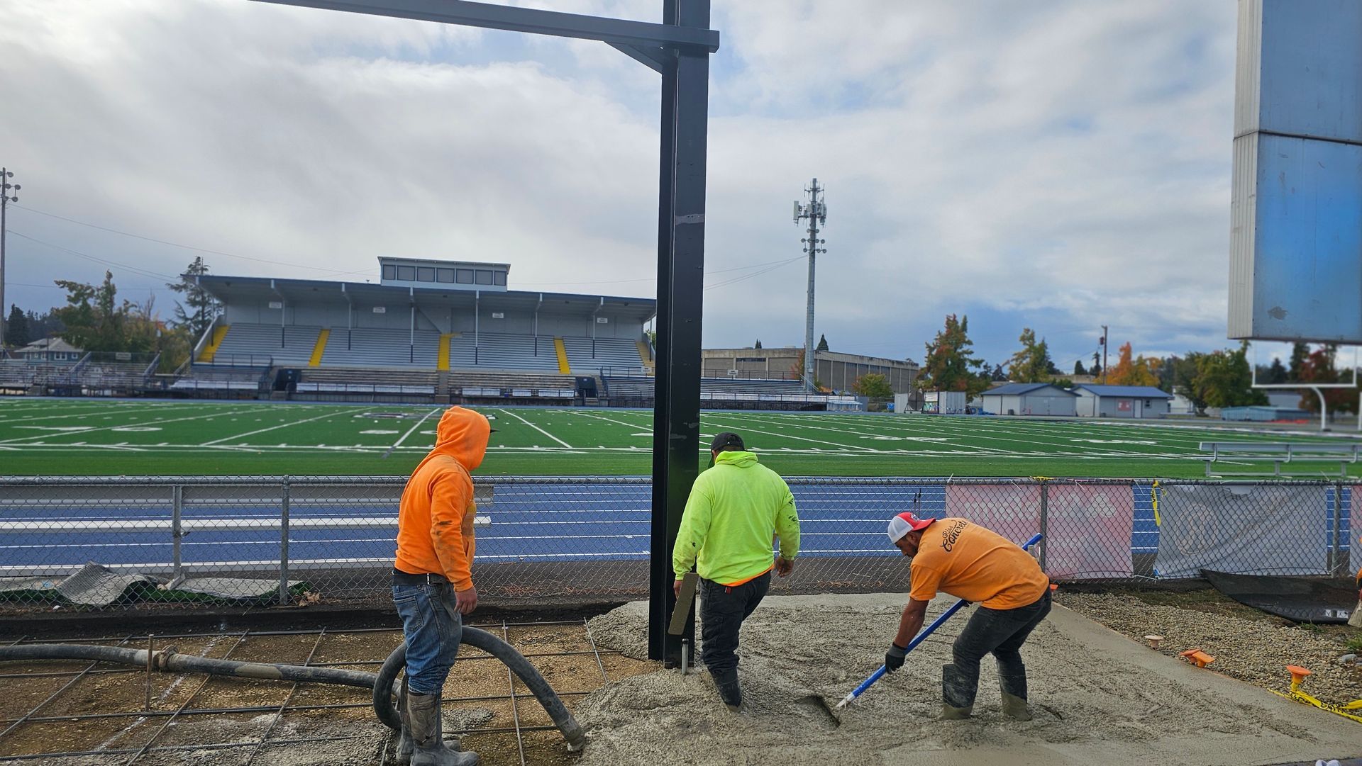 Concrete pumping crew pouring slab foundation near sports field with precision equipment
