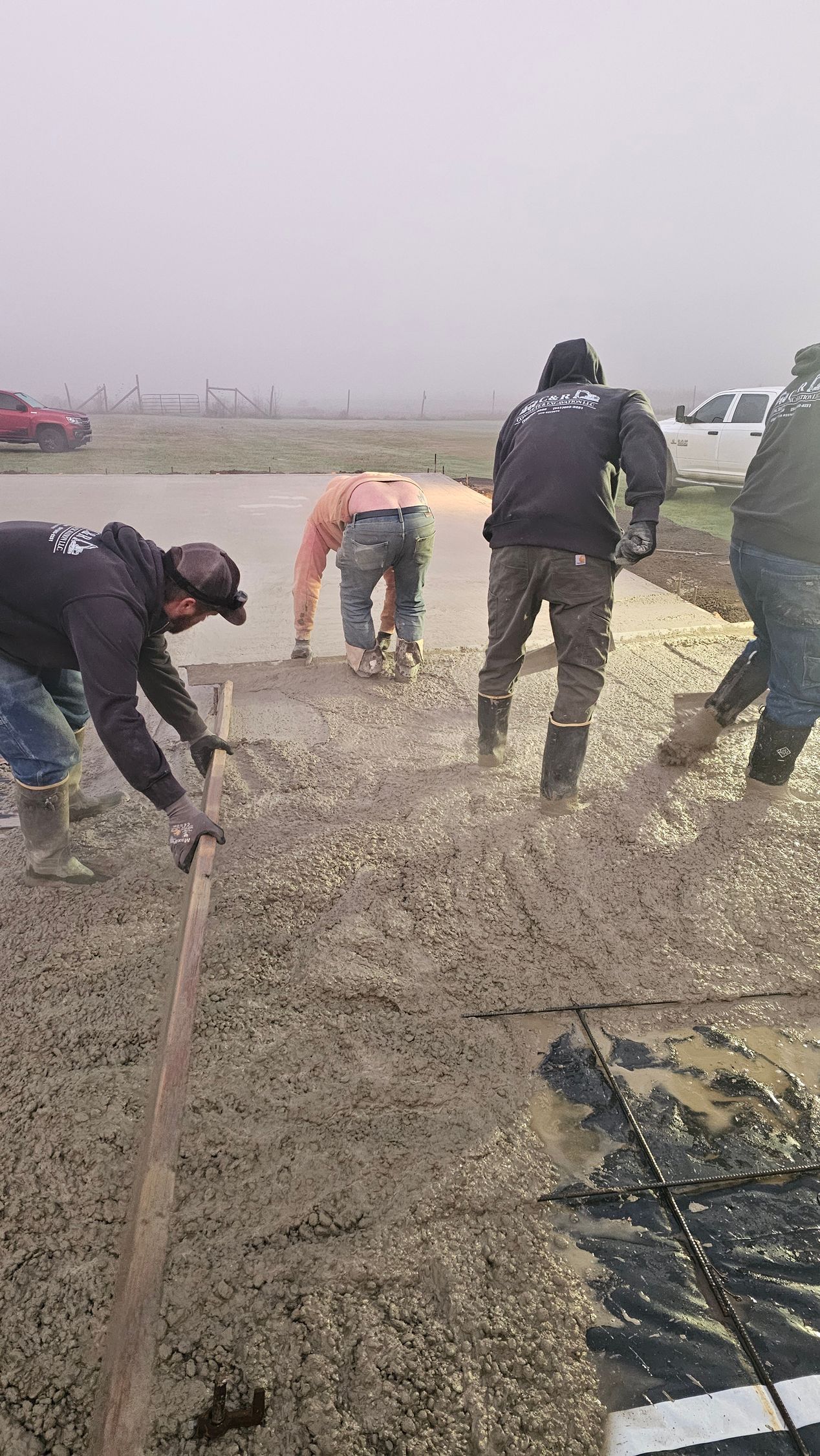 Concrete crew pouring and leveling slab during foggy morning residential job