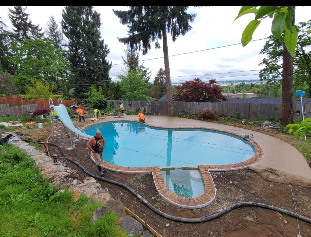 Concrete pool deck installation using pump hose with workers finishing the edge