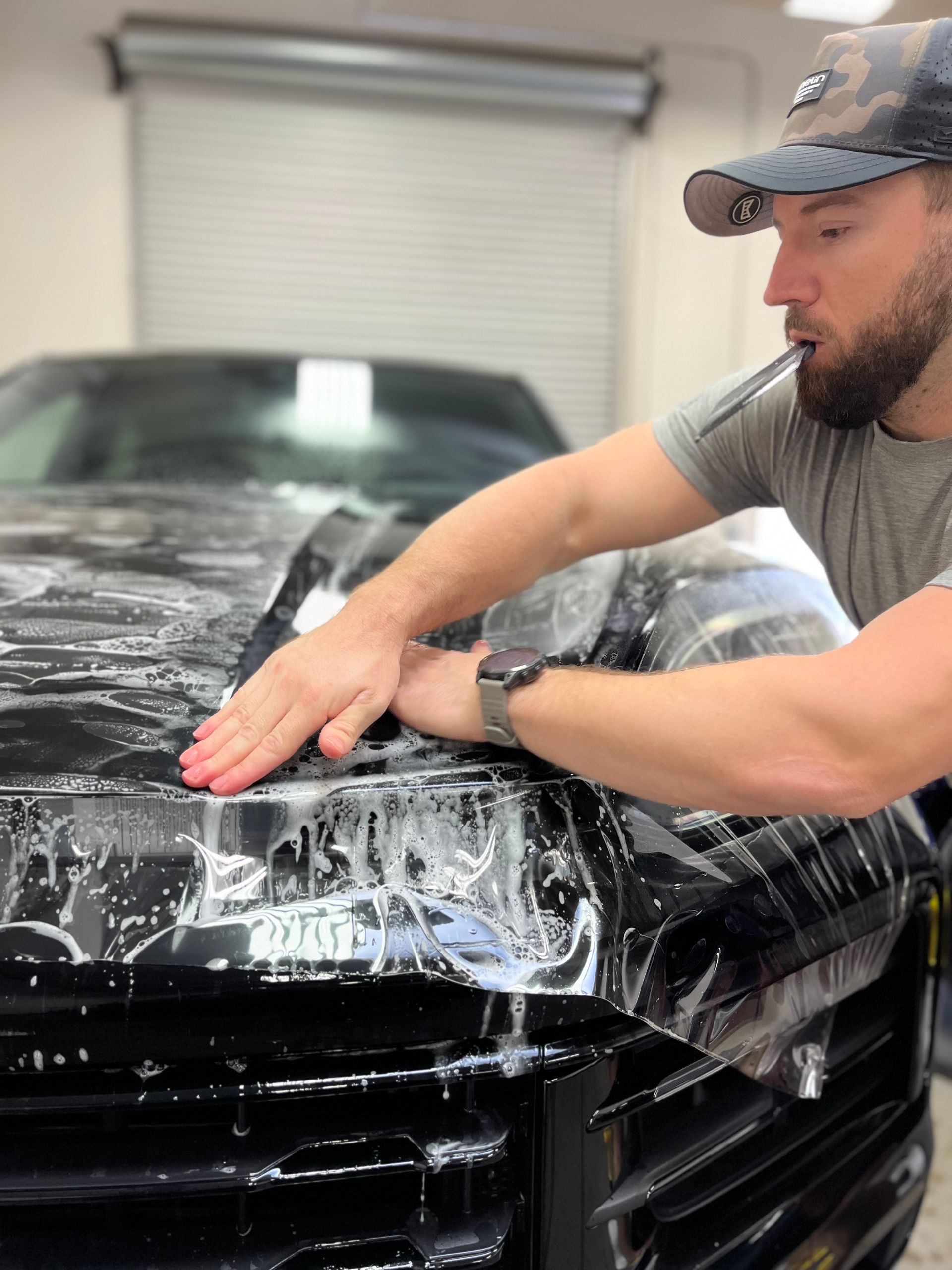 A man is covering the hood of a black truck with plastic wrap.