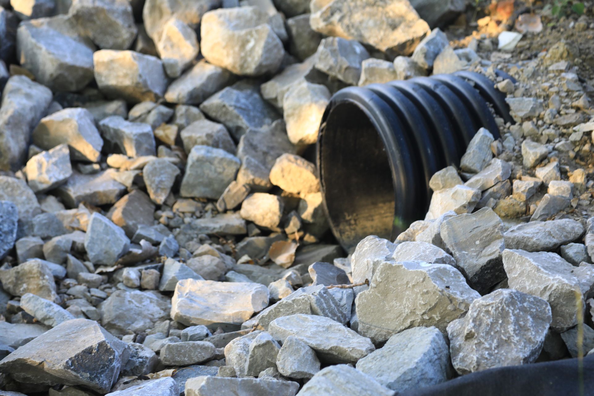 A black pipe is coming out of a pile of rocks.
