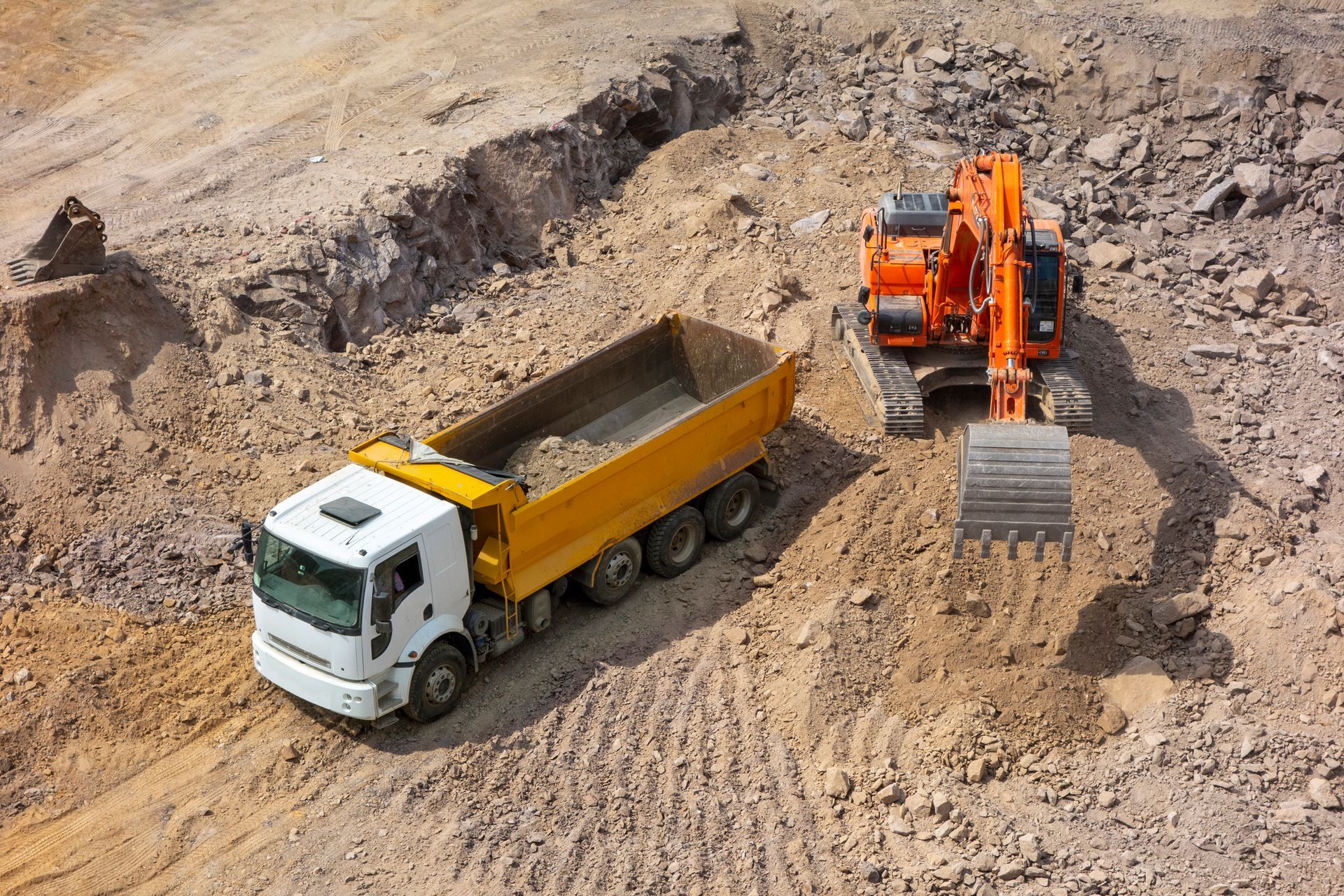 A dump truck is driving down a dirt road next to an excavator.