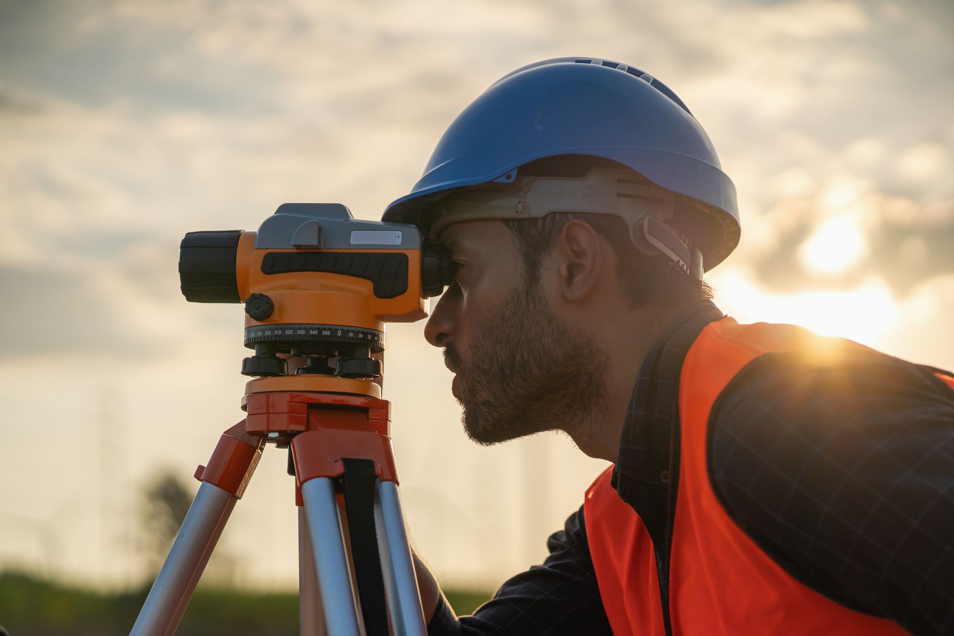 A man in a hard hat is looking through a level on a tripod.