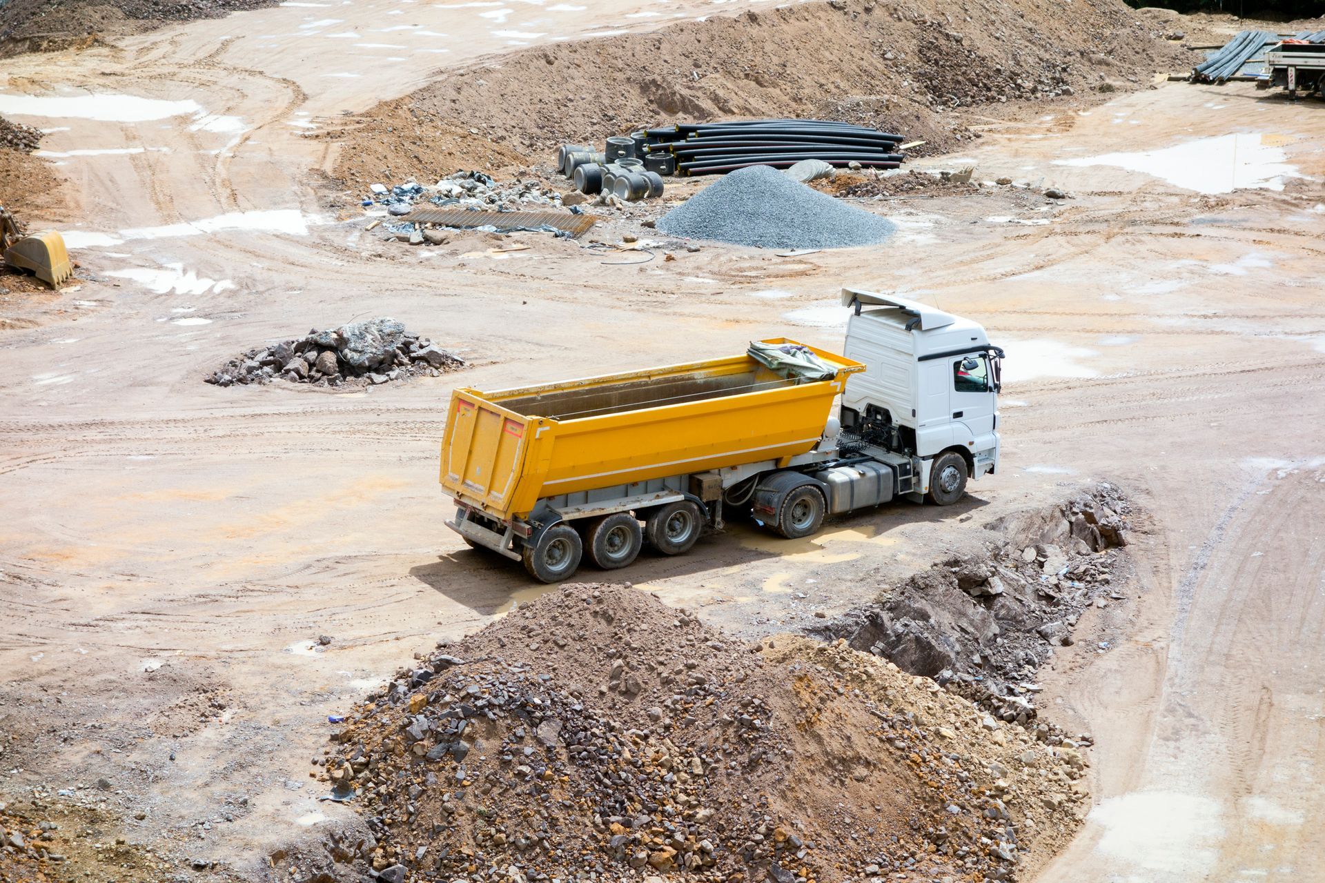 A dump truck is driving down a dirt road in a construction site.