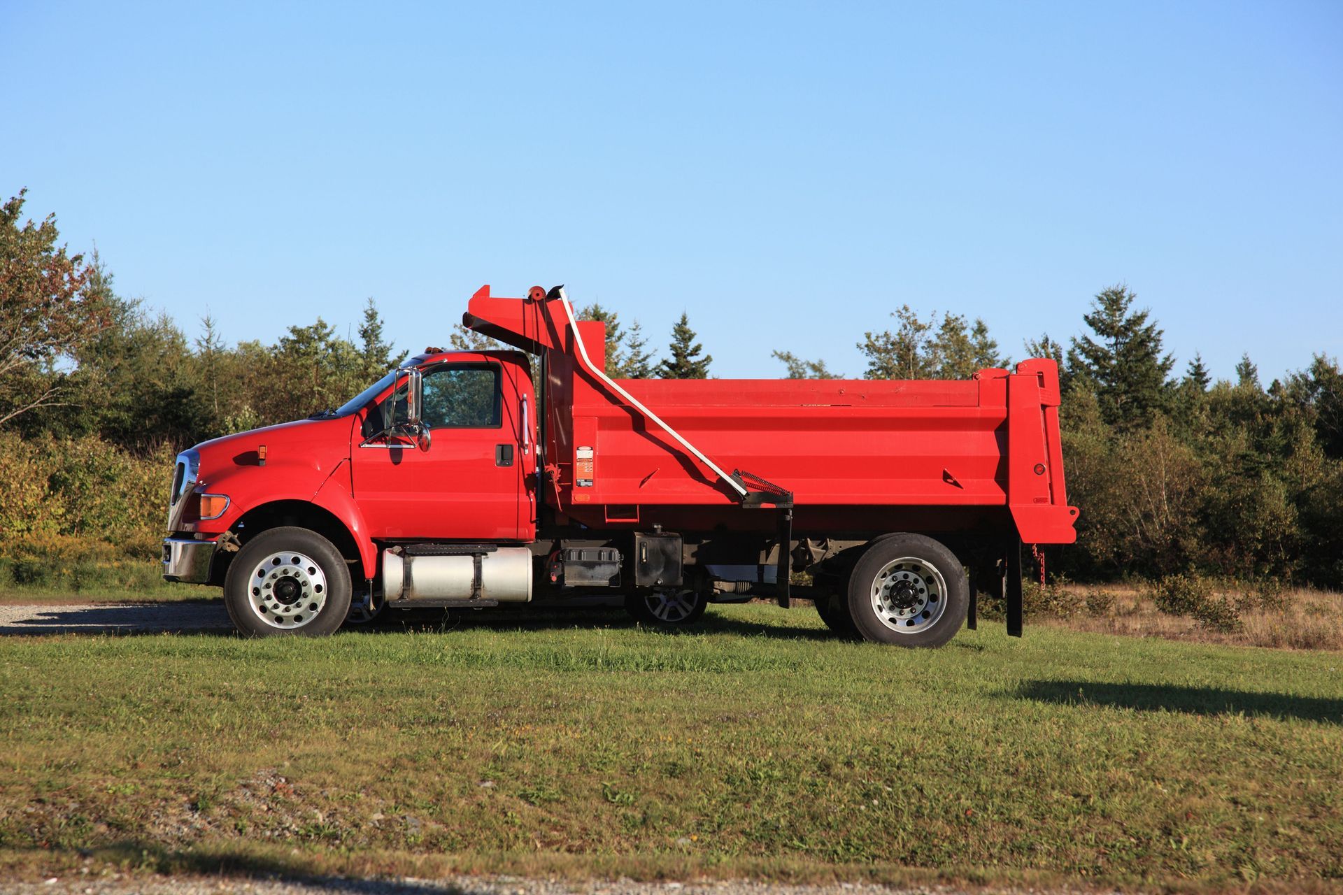 A red dump truck is parked in a grassy field.