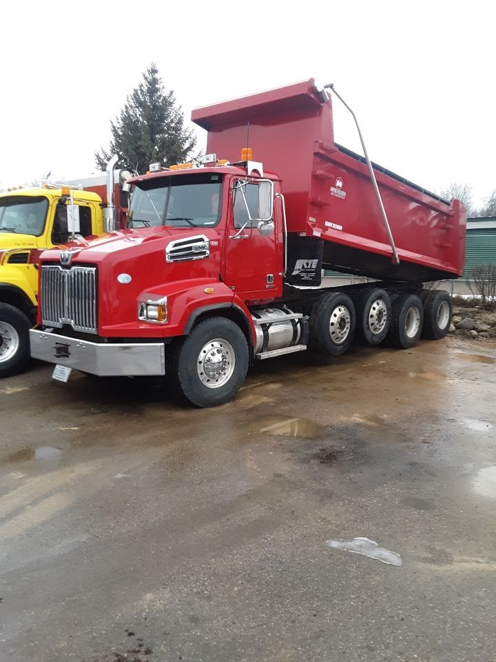 A yellow dump truck is driving down a dirt road.