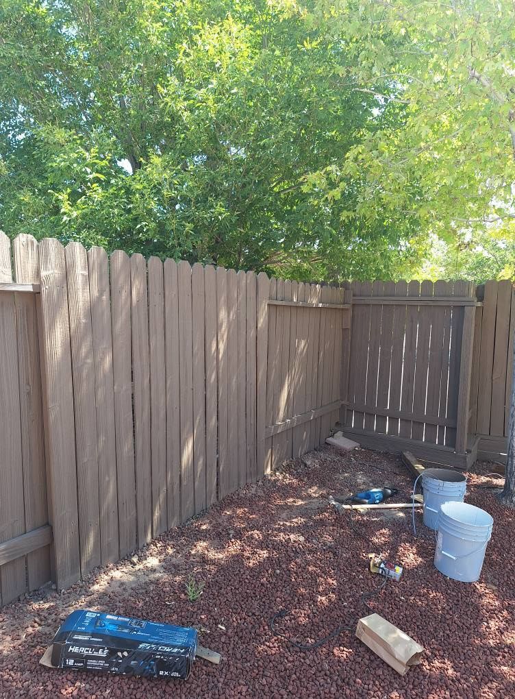 A section of a wooden privacy fence under construction in a yard with mulch, two buckets, and building supplies.