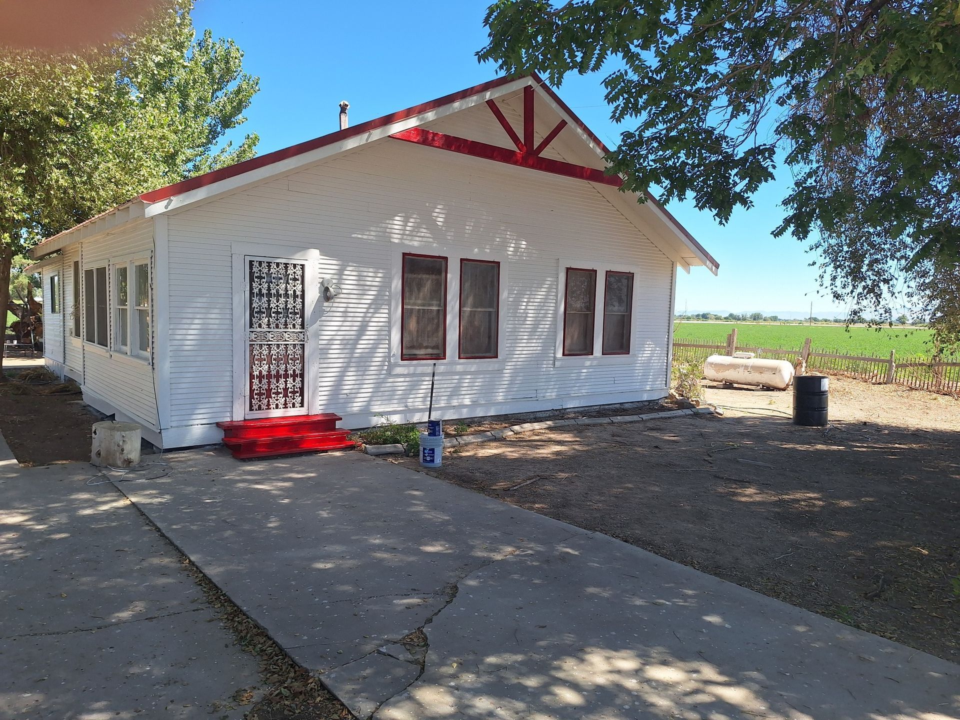 White one-story house with red trim, a decorative metal security screen door, and a concrete driveway, in a rural setting.