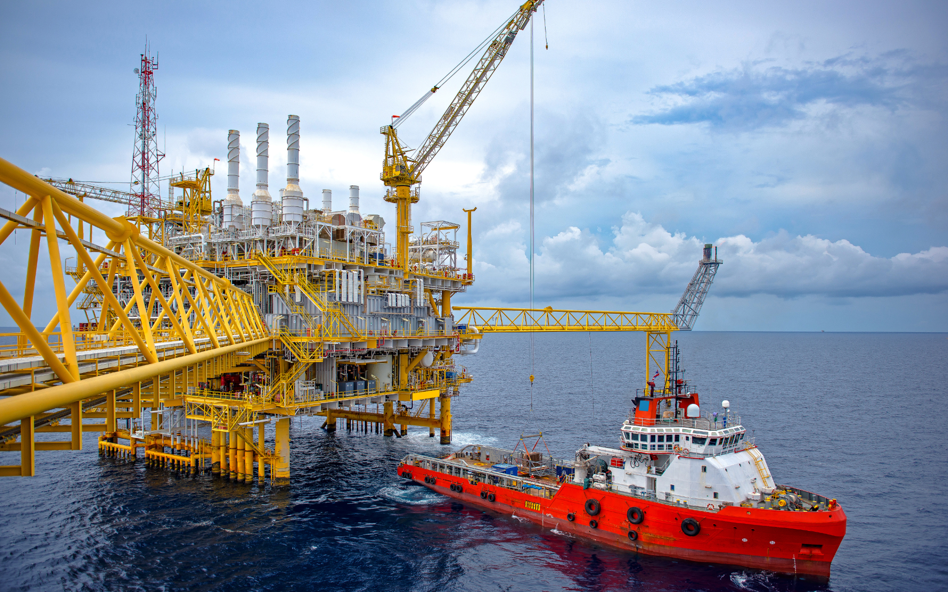 A tug boat is pulling a large oil rig in the ocean.