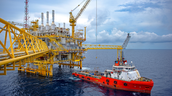 A tug boat is pulling a large oil rig in the ocean.