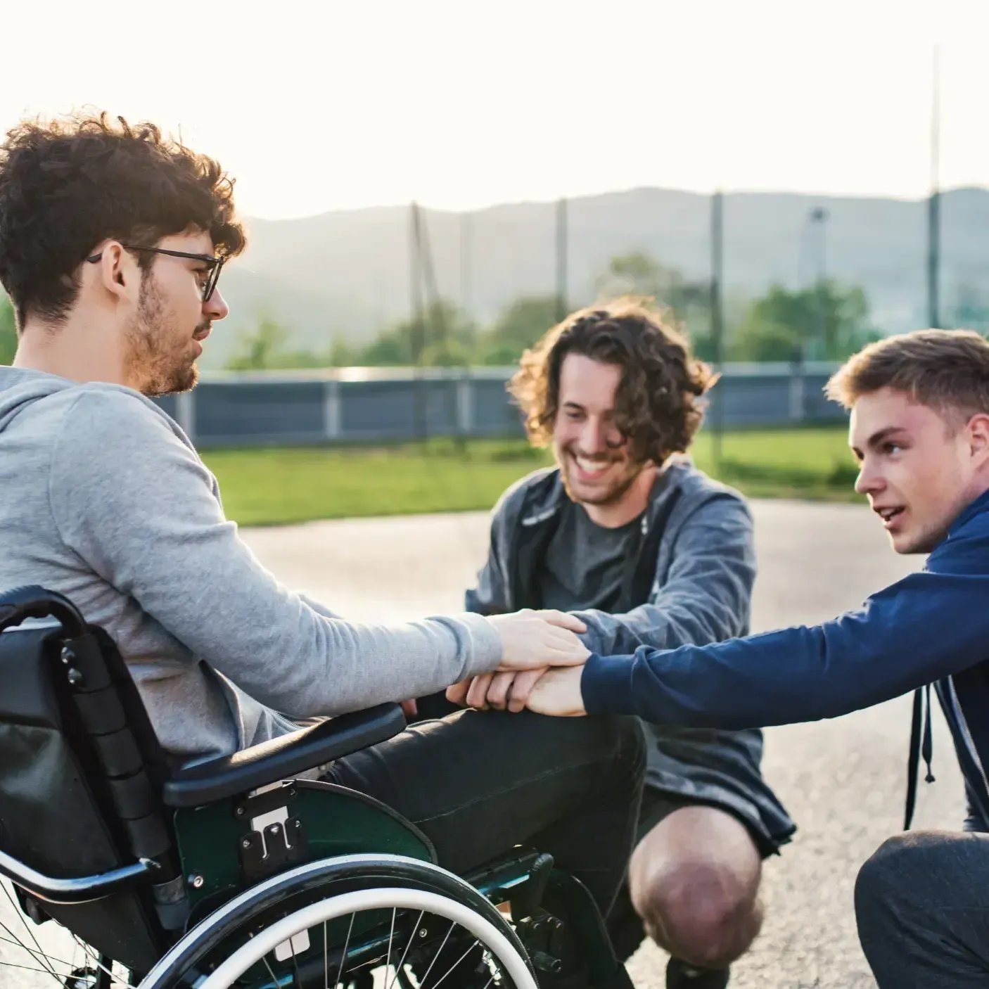 A man in a wheelchair is putting his hands together with two other men.