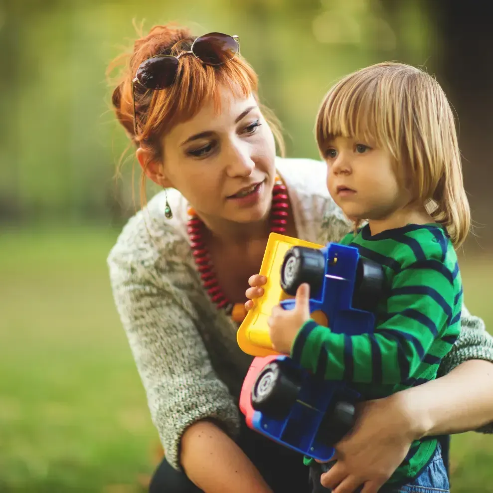 A woman is holding a little boy who is holding a toy truck.