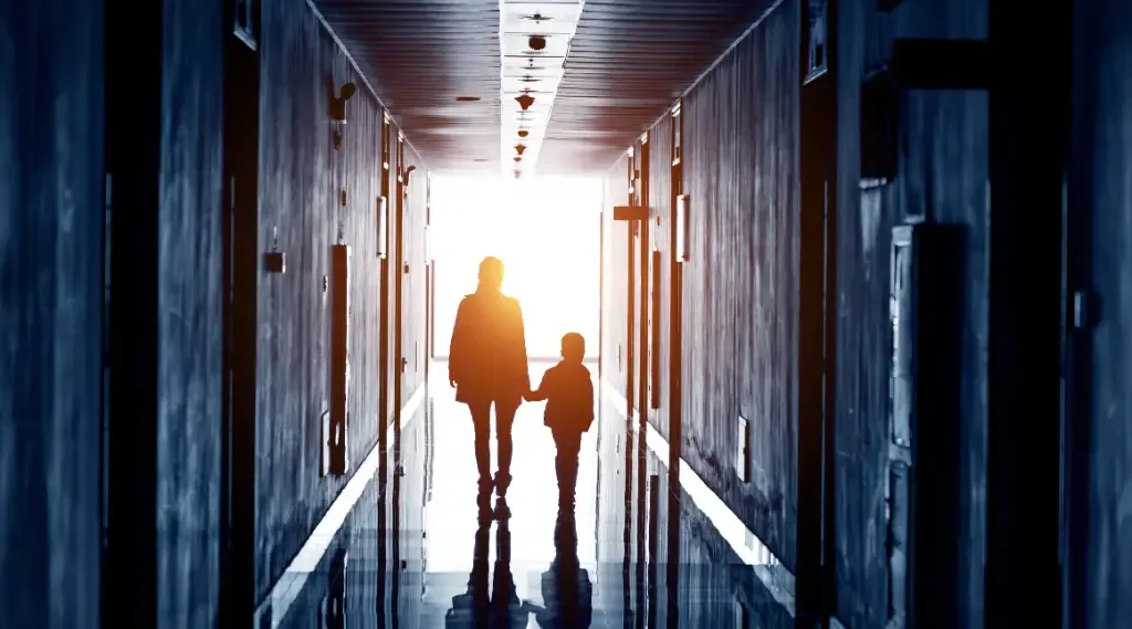 A man and a child are walking down a hallway holding hands.
