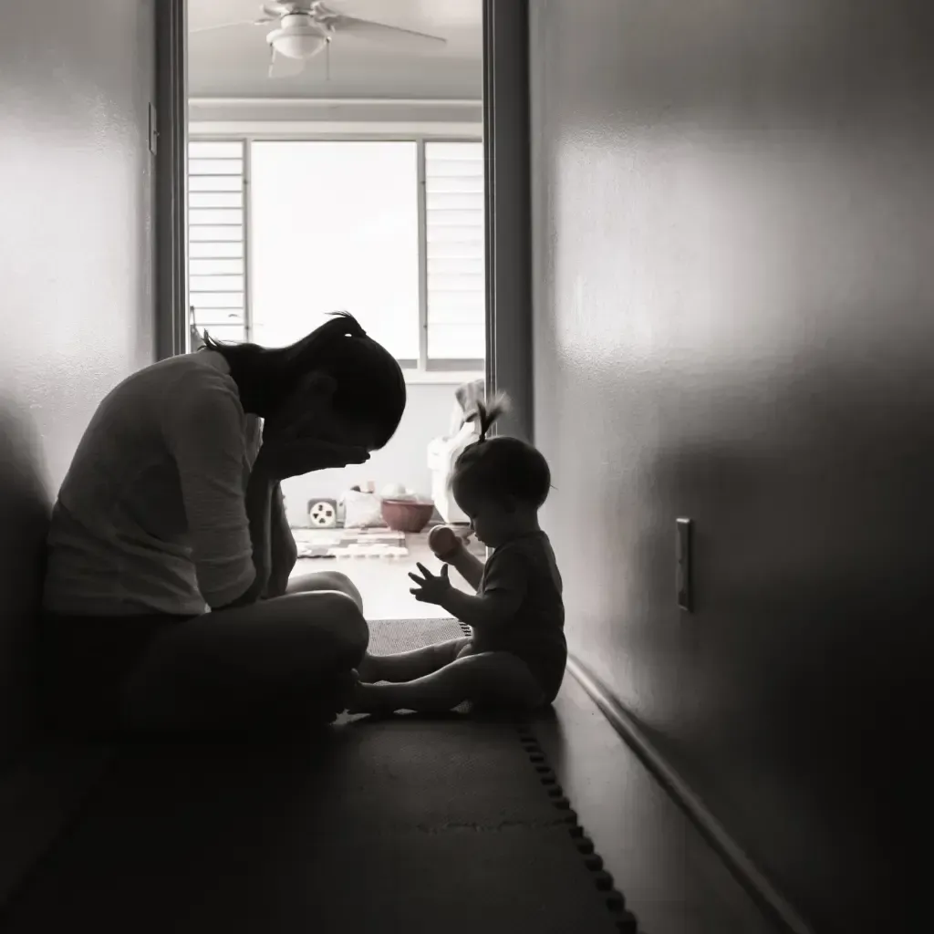 A woman is kneeling down next to a baby in a hallway