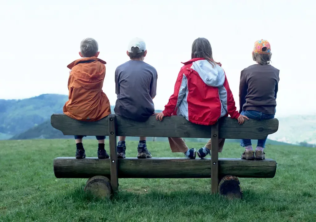 Four children are sitting on a wooden bench looking at the mountains