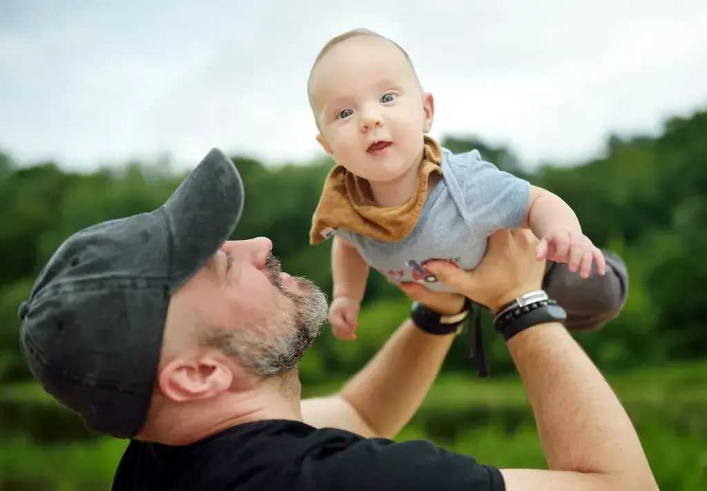A man is holding a baby in his arms in the air.