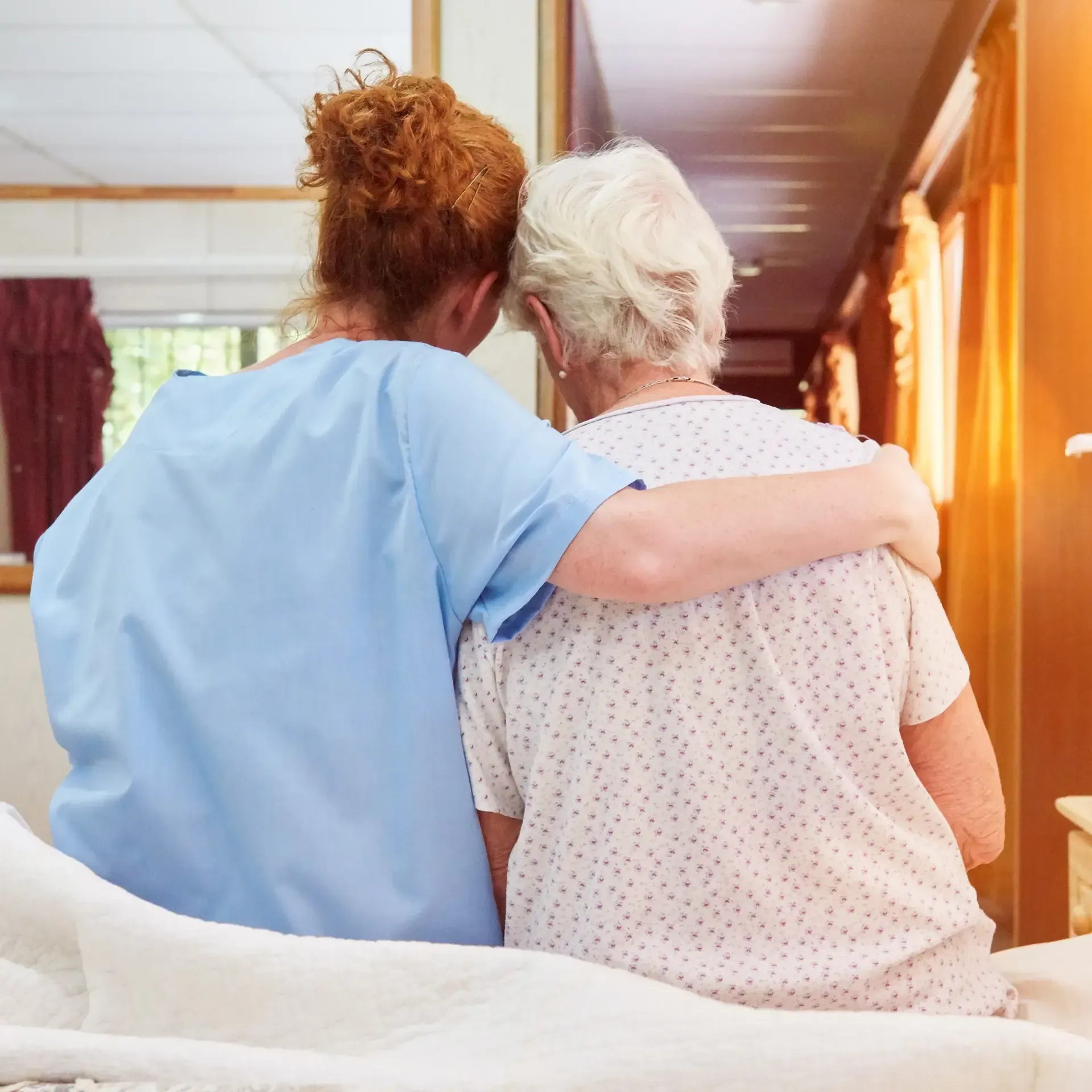 A nurse is hugging an elderly woman in a hospital bed