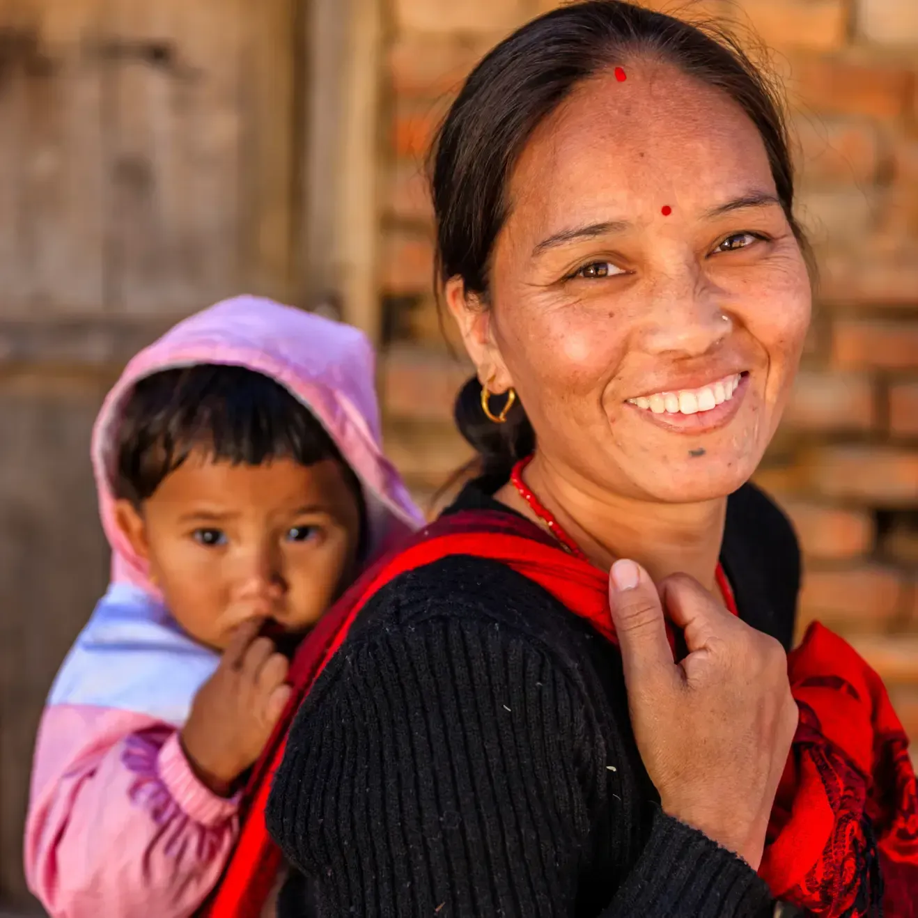 A woman is smiling while carrying a baby on her back
