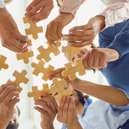 A group of people are holding wooden puzzle pieces in their hands