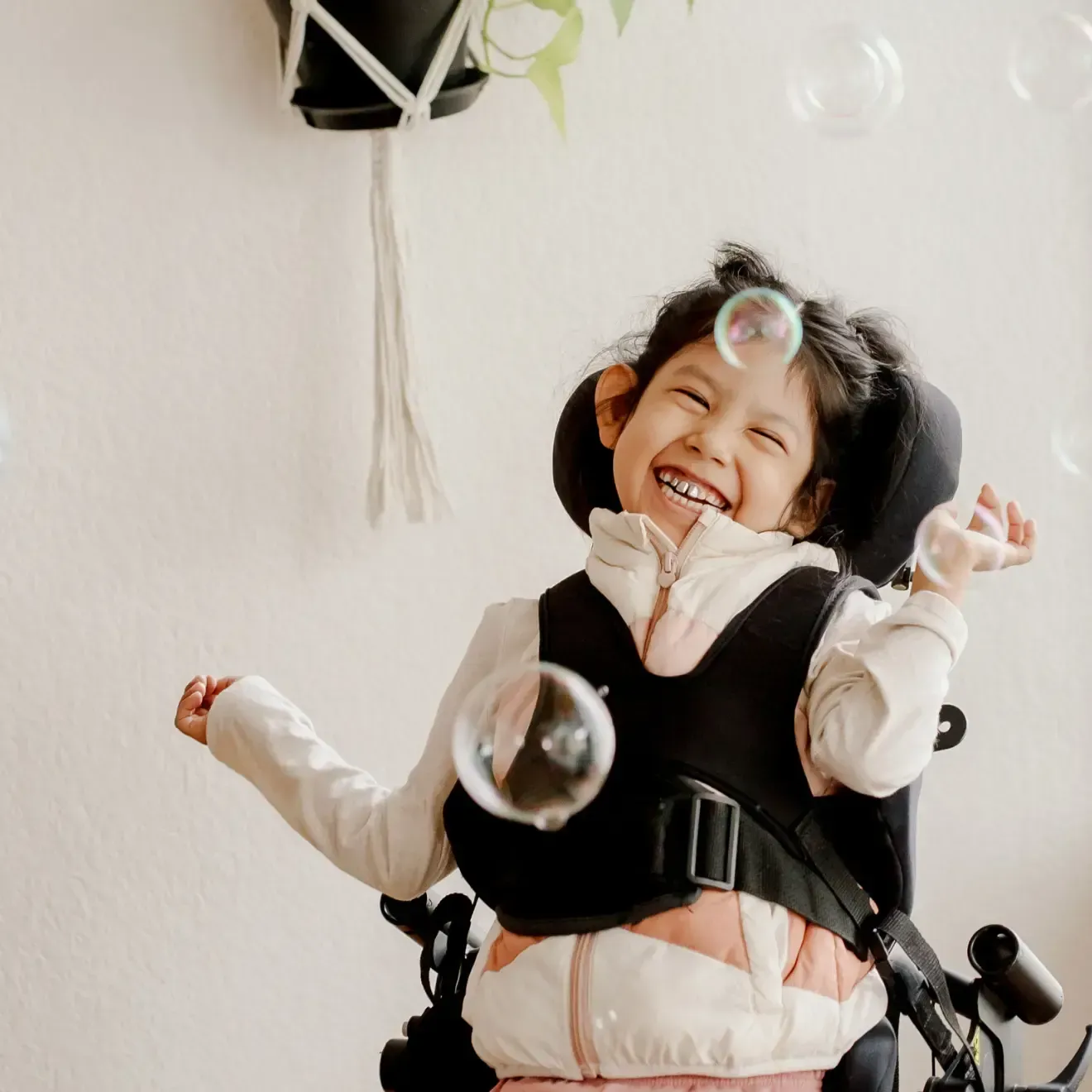 A little girl in a wheelchair is playing with soap bubbles