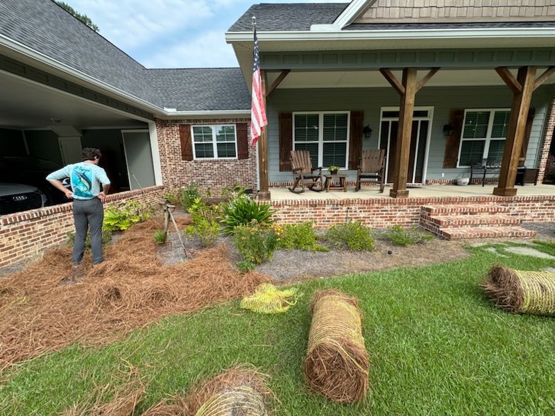 A man is standing in front of a house with hay bales in the yard.