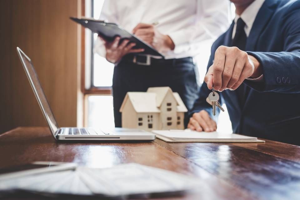 Business meeting with laptop, model house, and keys on a desk