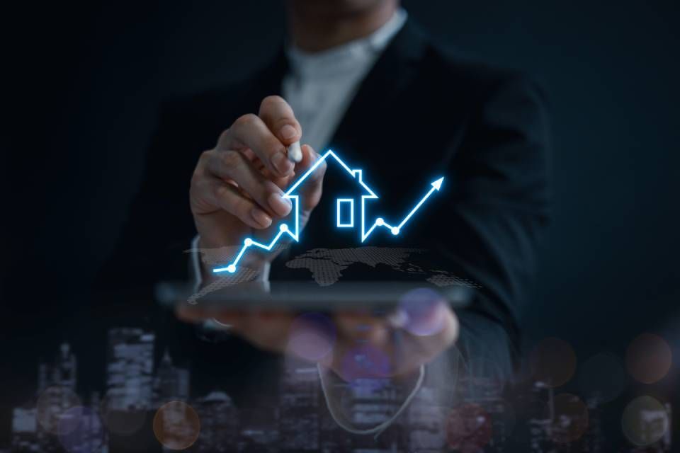 Person holding a tablet with a glowing blue house and rising stock chart, city skyline blurred behind