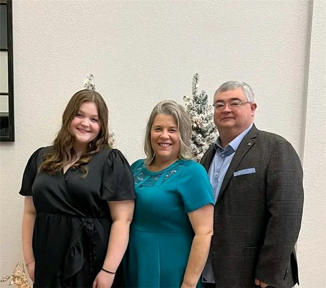 2 adults smiling in front of the pulpit with smaller photographs of them hugging children