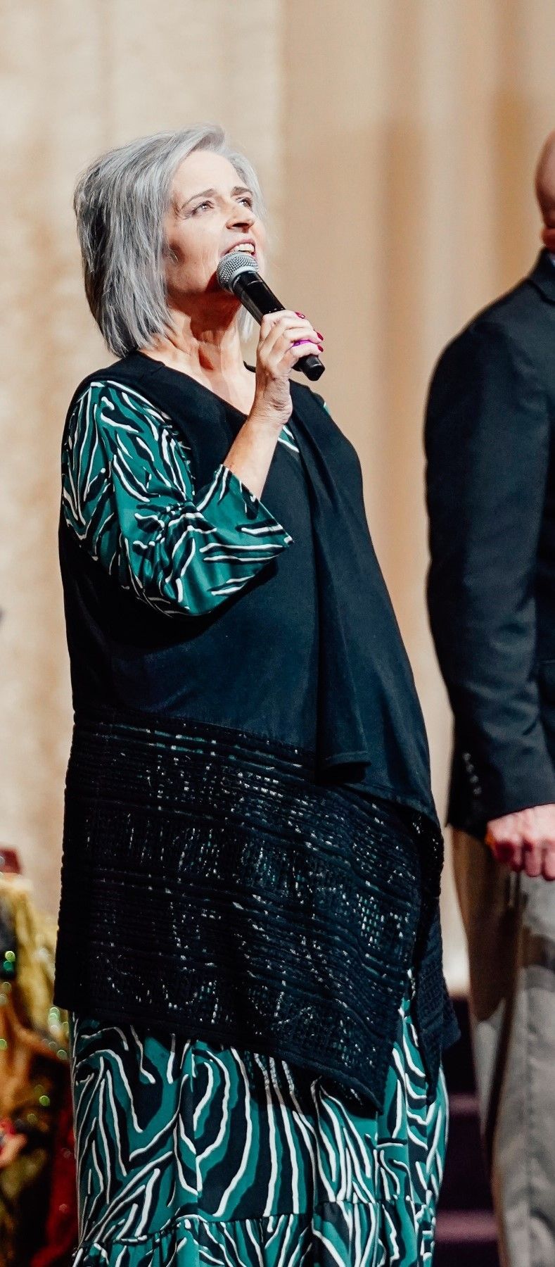 lady holding microphone lokin up standing beside a gentleman in suite