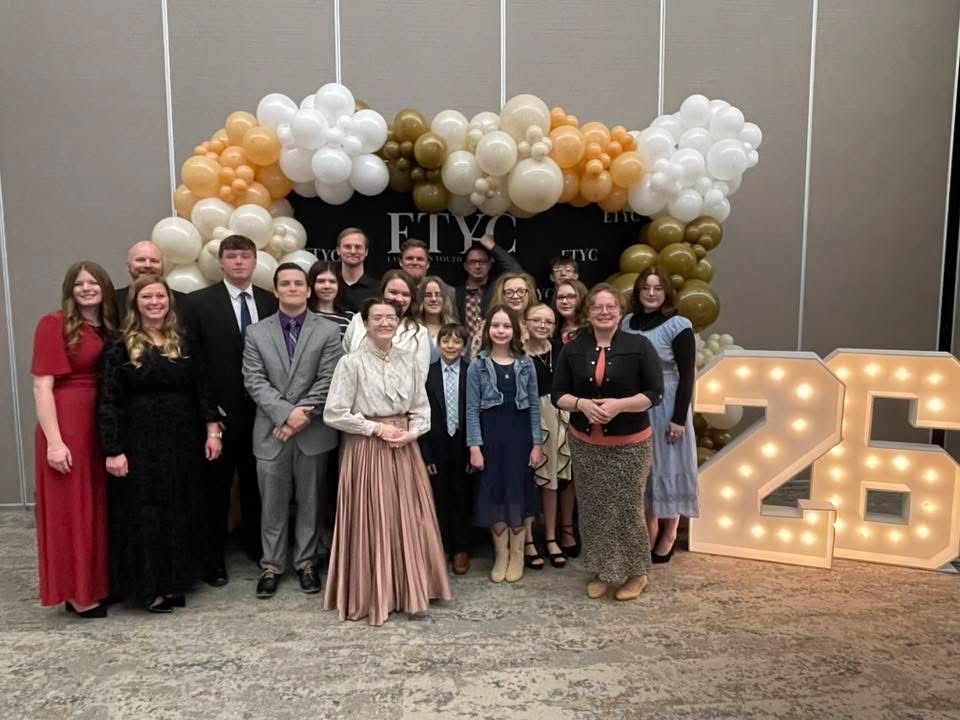 Group of people posing for a photo in front of a balloon arch and light-up 