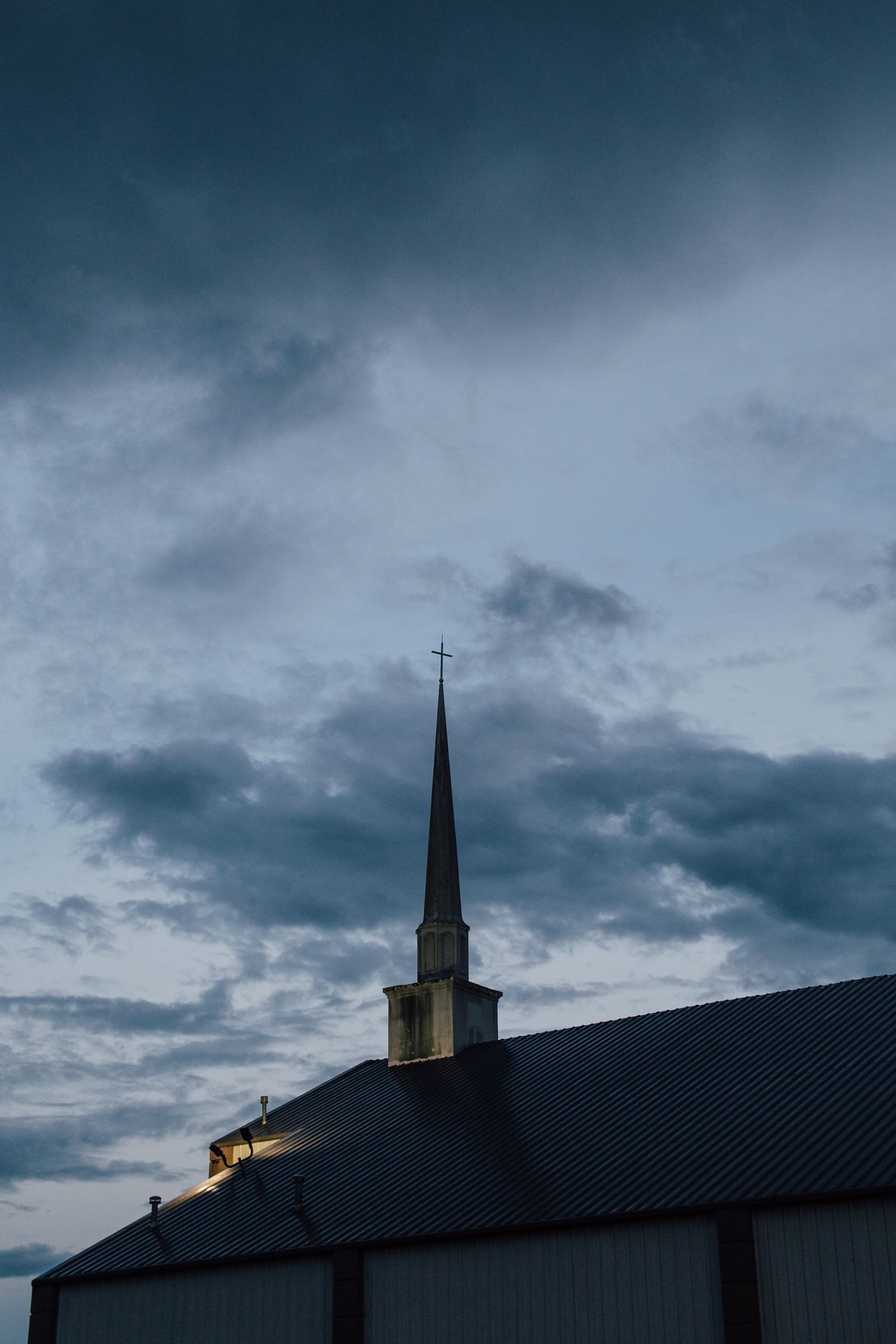 A church steeple with a cross on top of it against a cloudy sky.