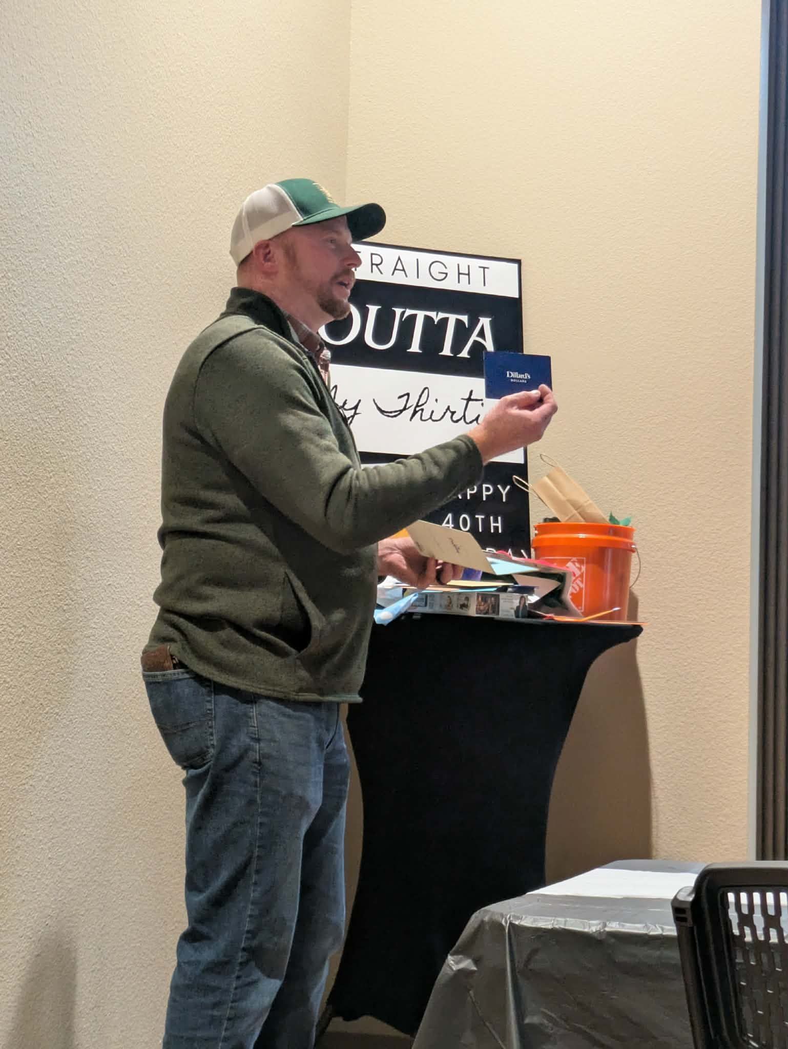 man in a cap holding a gift card beside a table of gifts