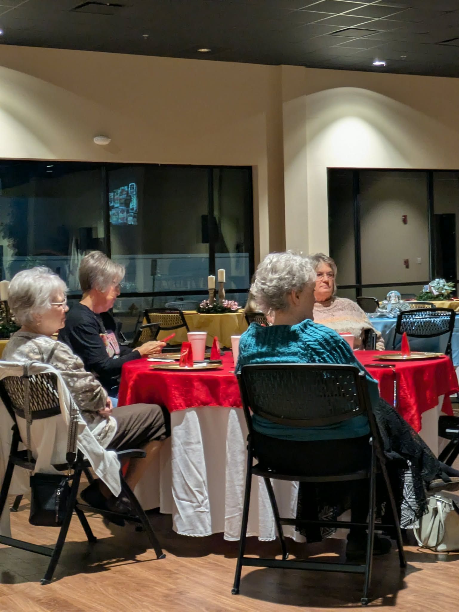 Four people seated at a table covered with a red tablecloth. They appear to be in a gathering.