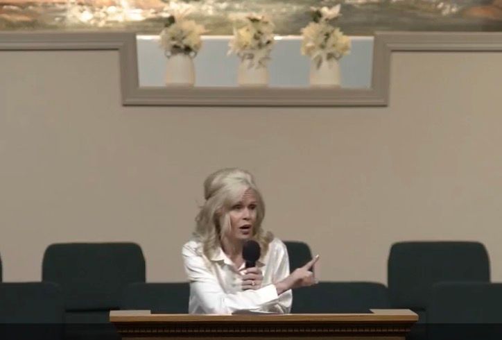 blond haired lady holding a mic and pointing. preaching