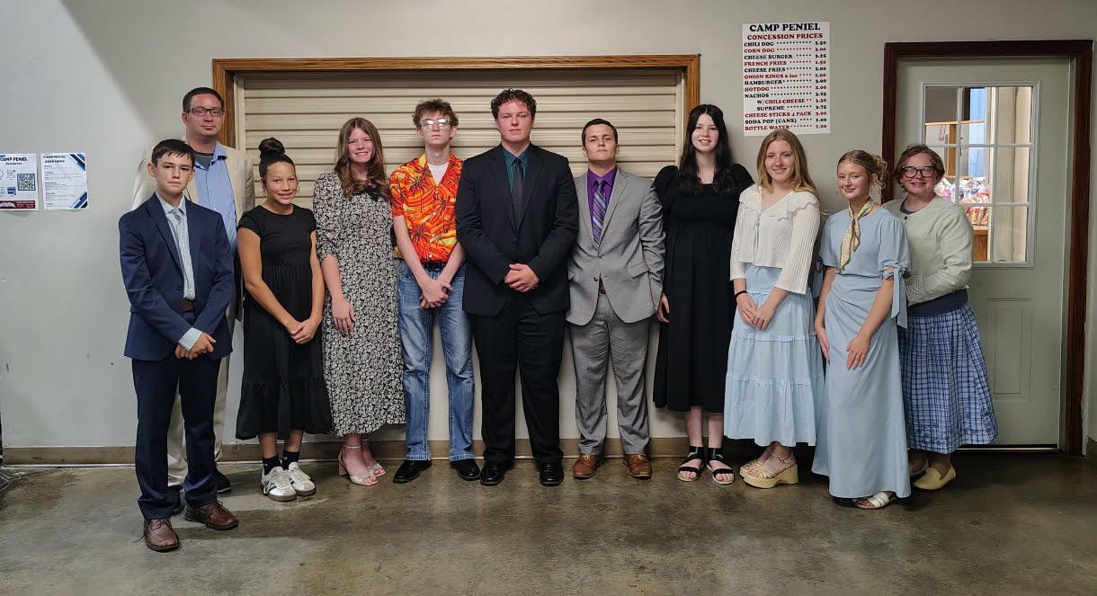 Ten people pose in a row indoors in front of framed wall decor and a mirror.