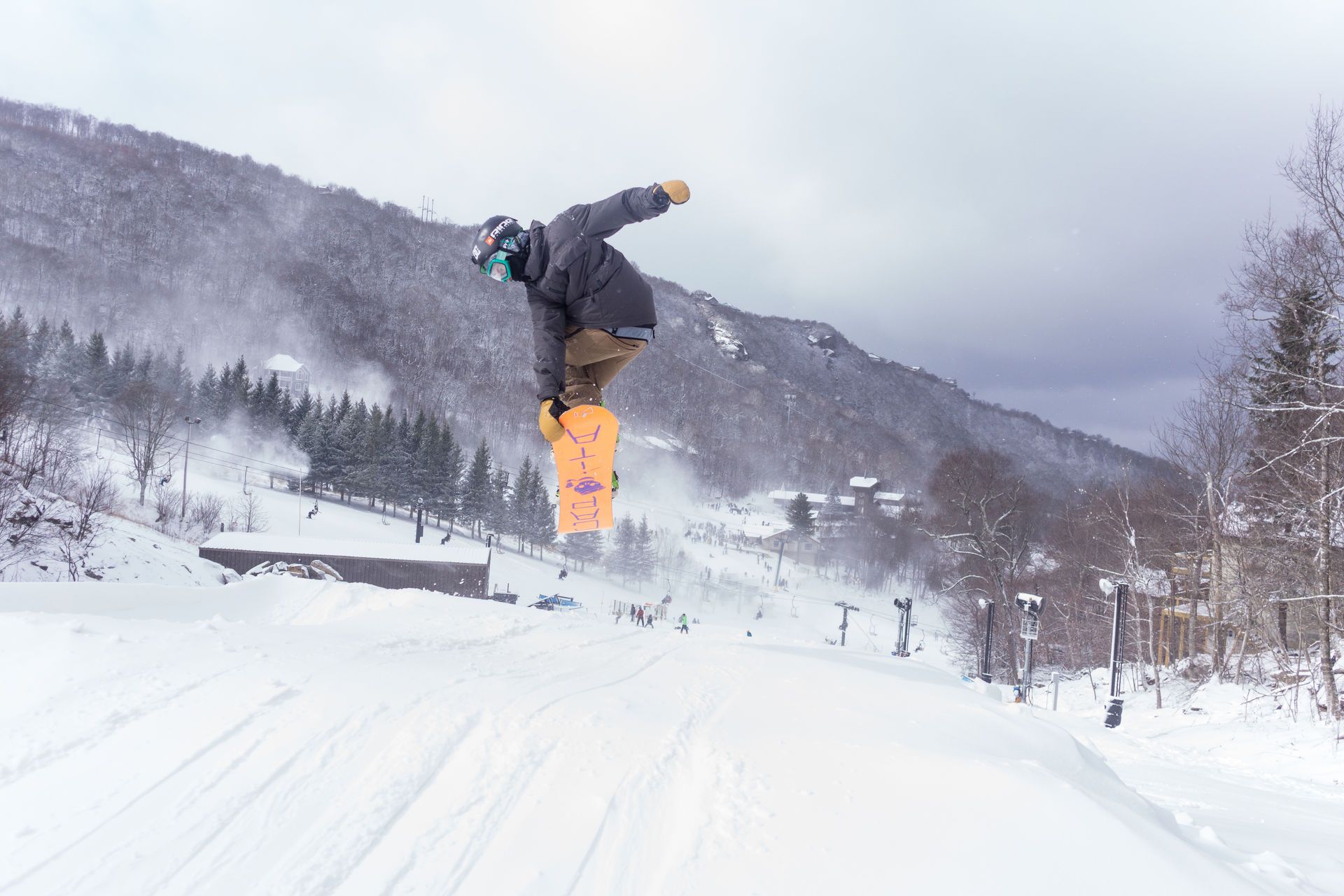 Snowboarder in mid-air performing a trick on a snowy jump with mountain backdrop.