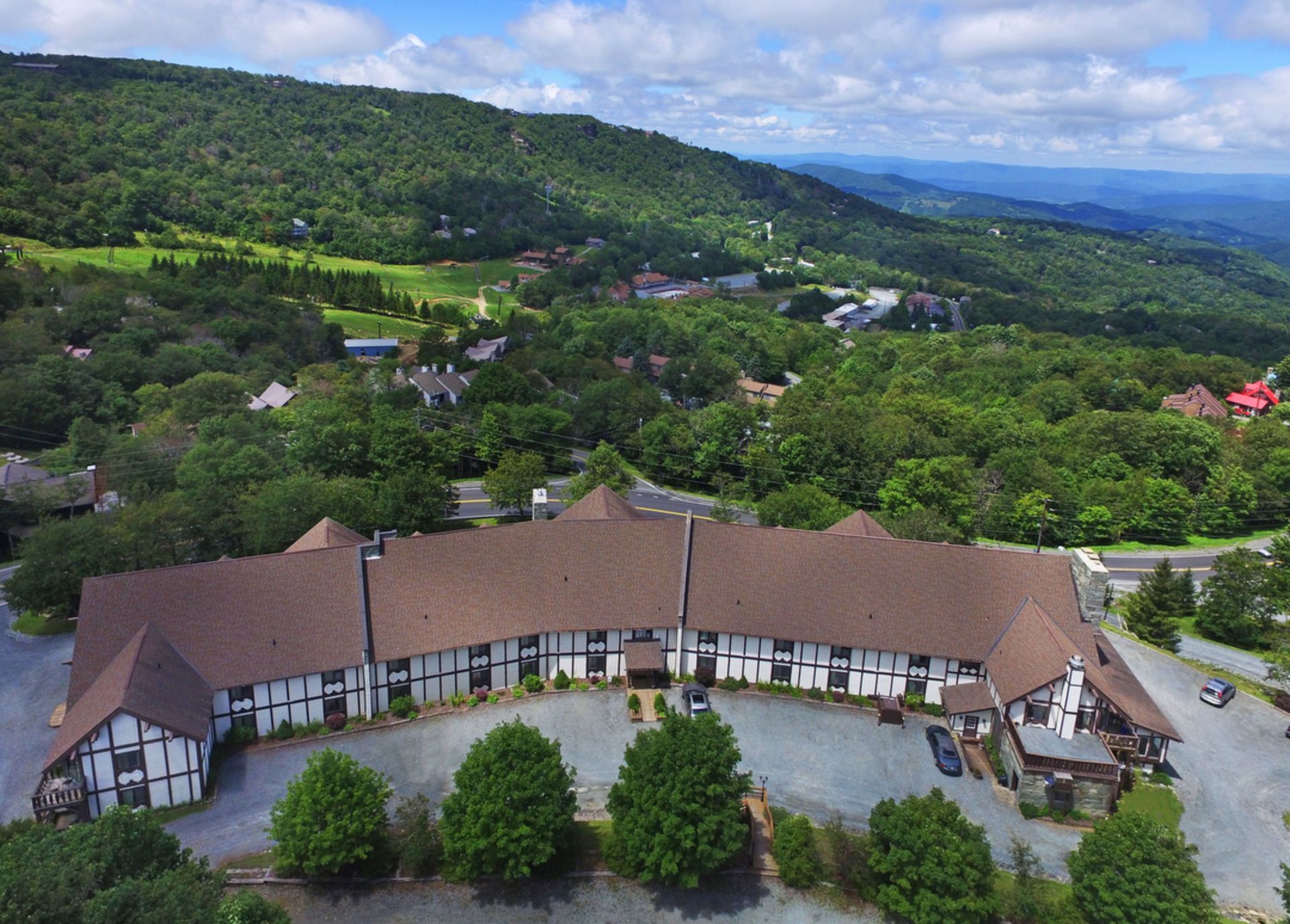 An aerial view of a brown and white building surrounded by trees, with a mountain in the background.