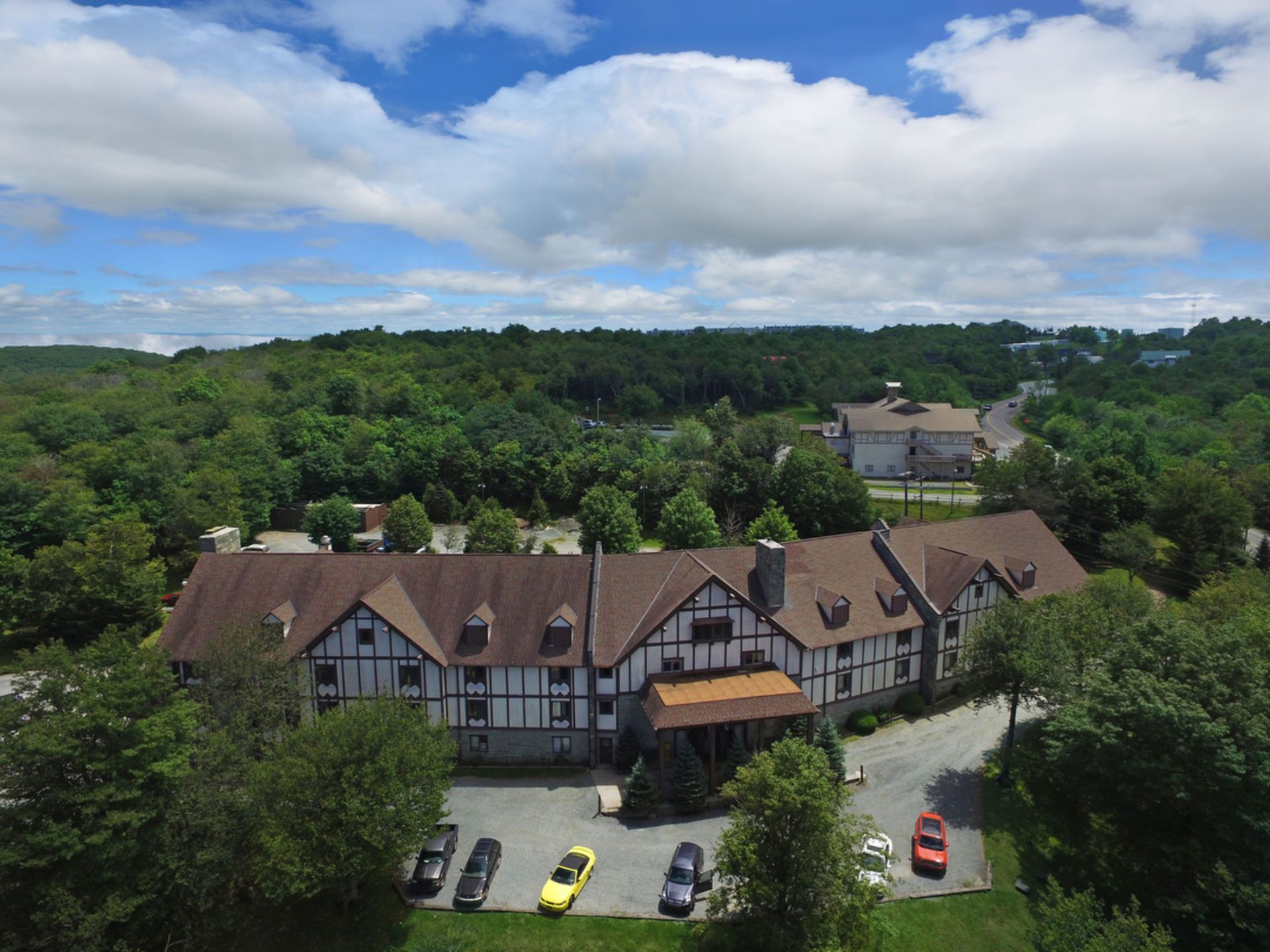 Hotel with brown roof, white and brown exterior, surrounded by trees, under a blue sky with clouds.