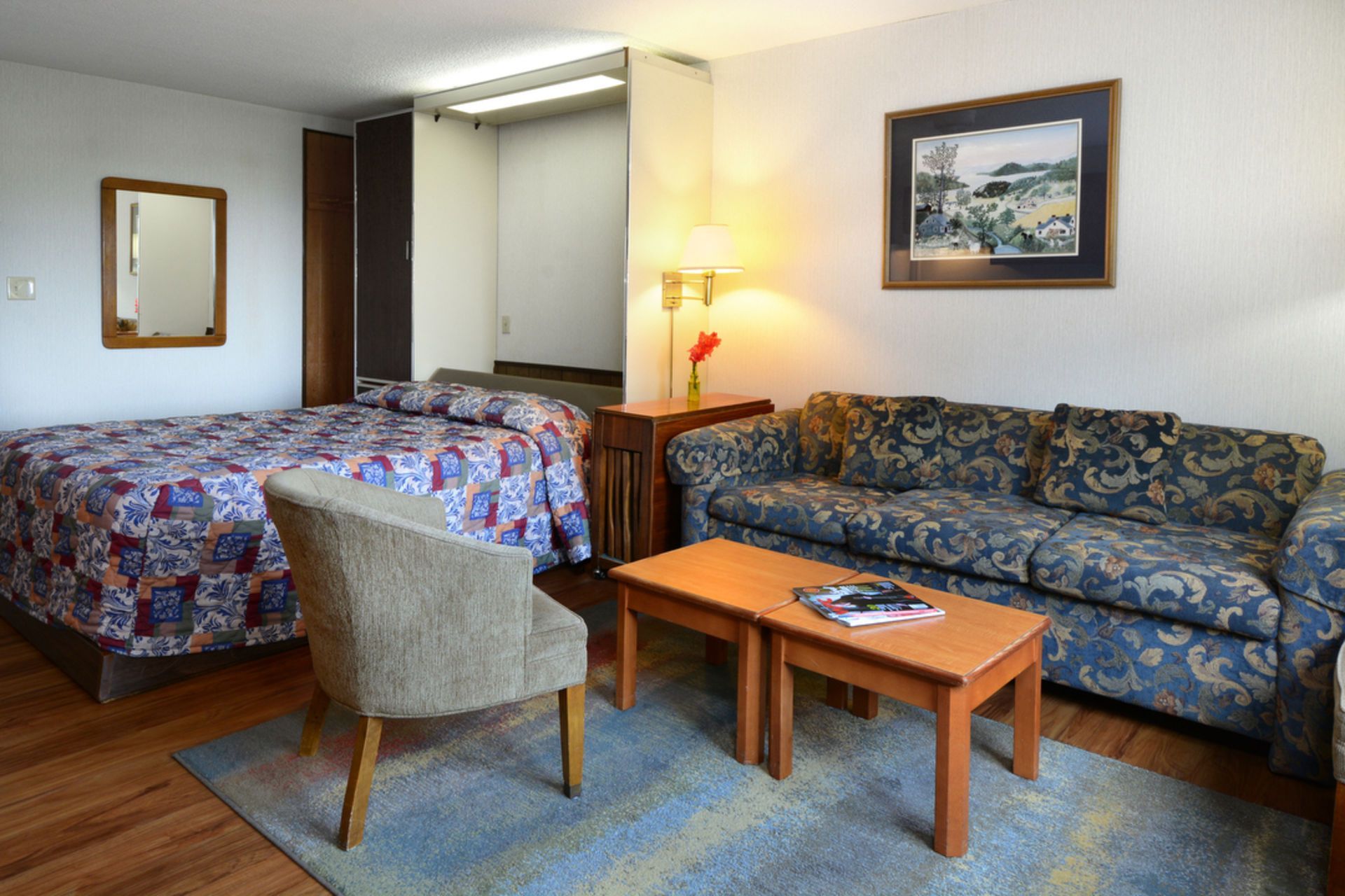 Hotel room with bed, couch, small table, and chair. Brown and blue patterned fabrics.