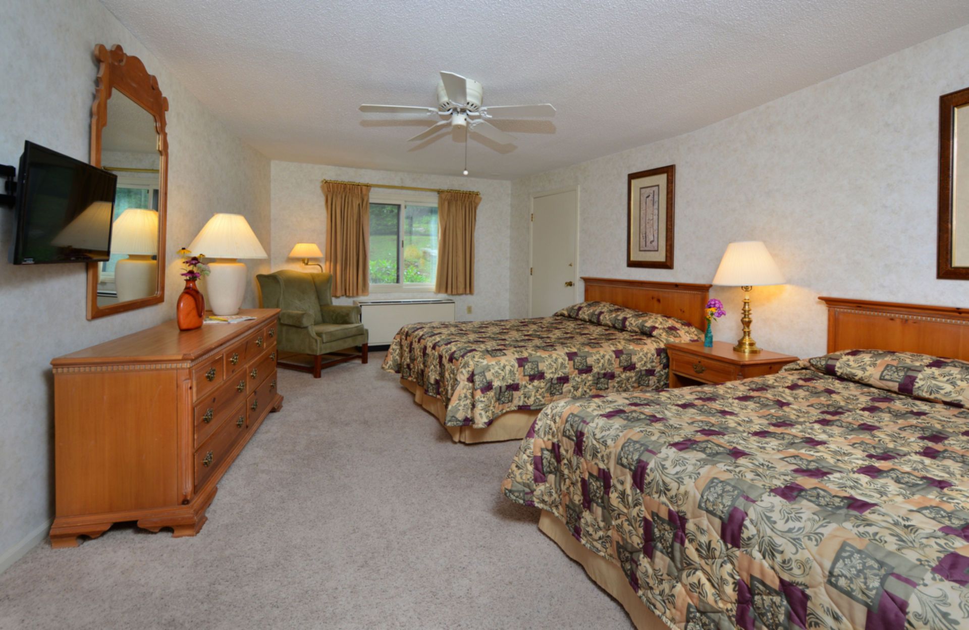 Hotel room with two beds, dresser, mirror, small chair, and a window.