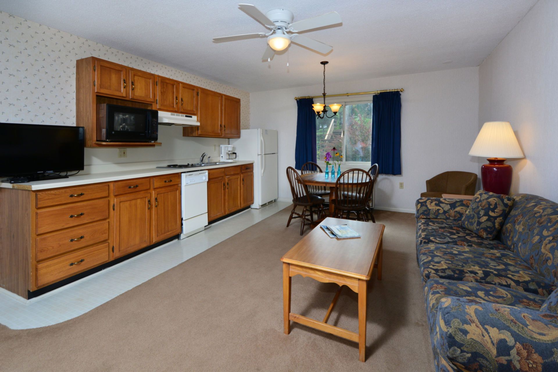 Cozy living space with kitchen. Wood cabinets, microwave, refrigerator, dining table, sofa, and lamp.