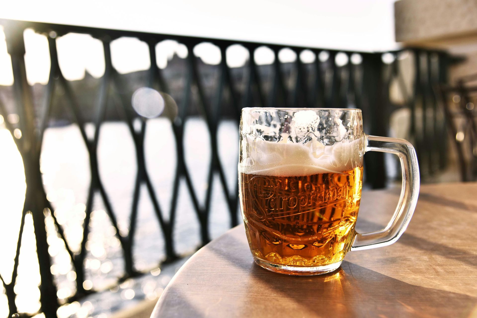 Glass mug of beer on a table, balcony view, sunny day.