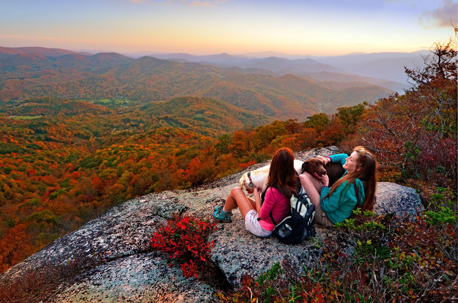 Two women and dog enjoy autumn mountain vista.