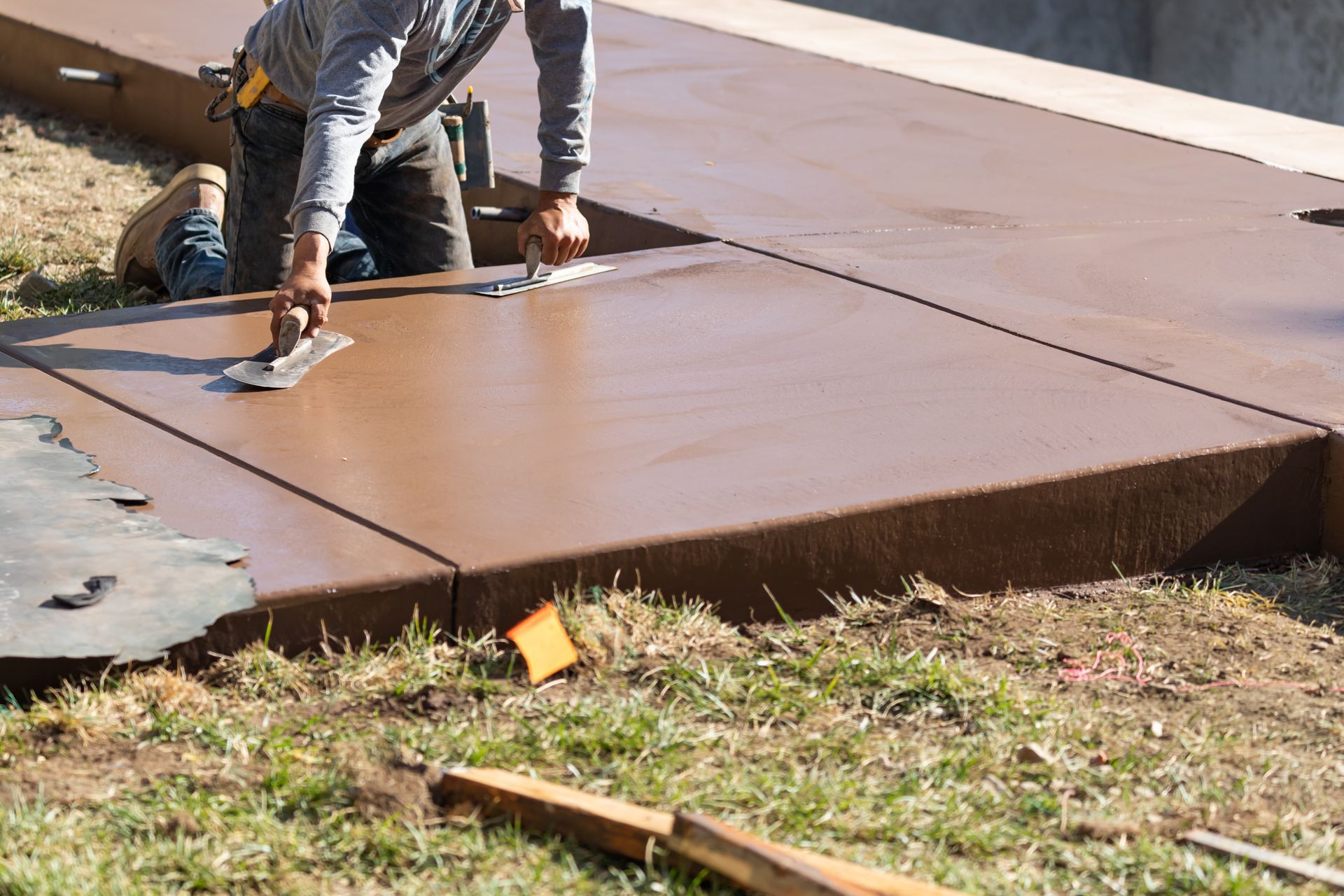 A man is working on a concrete walkway with a trowel.