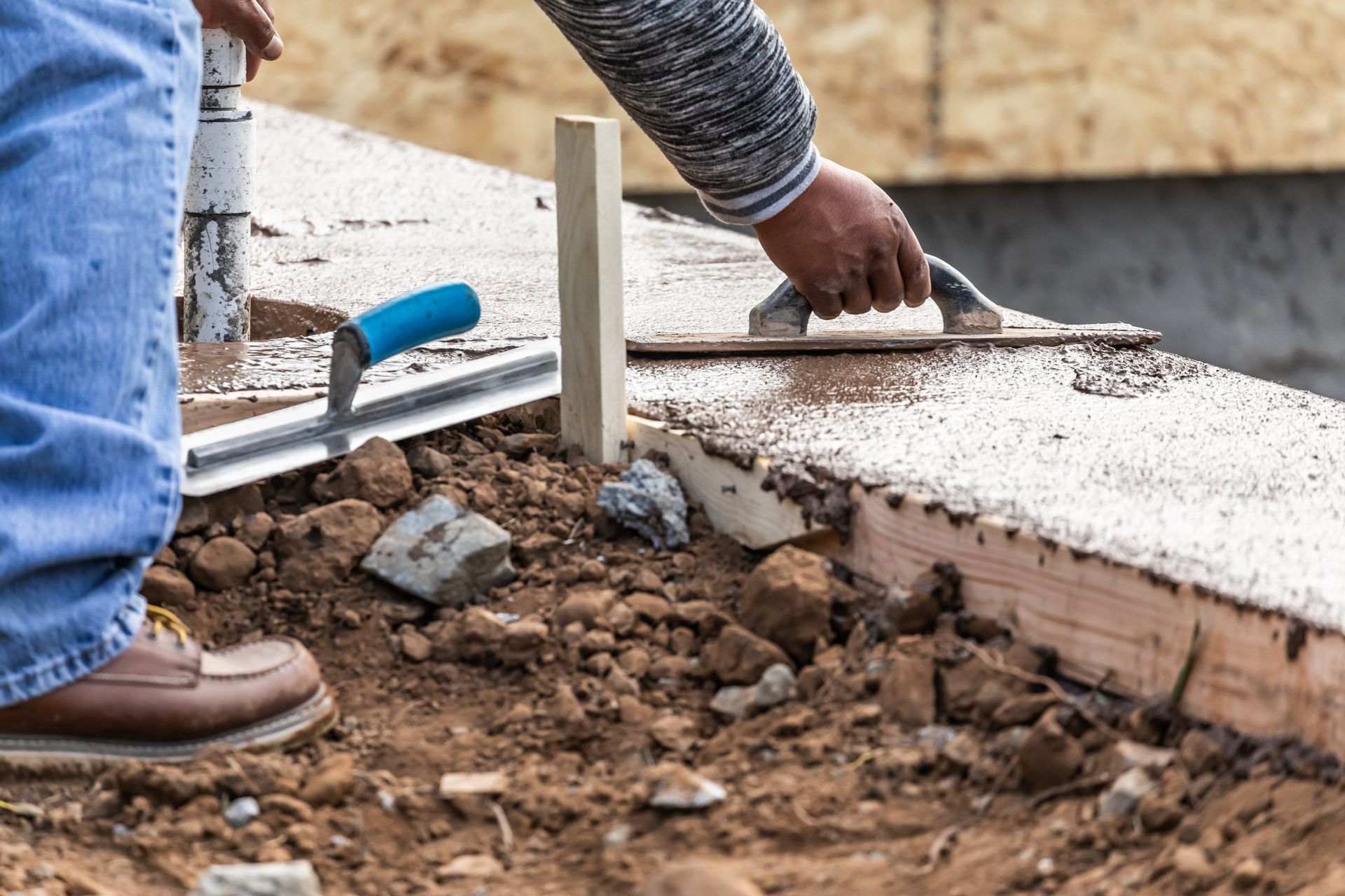 A man is using a trowel to spread concrete on a sidewalk.