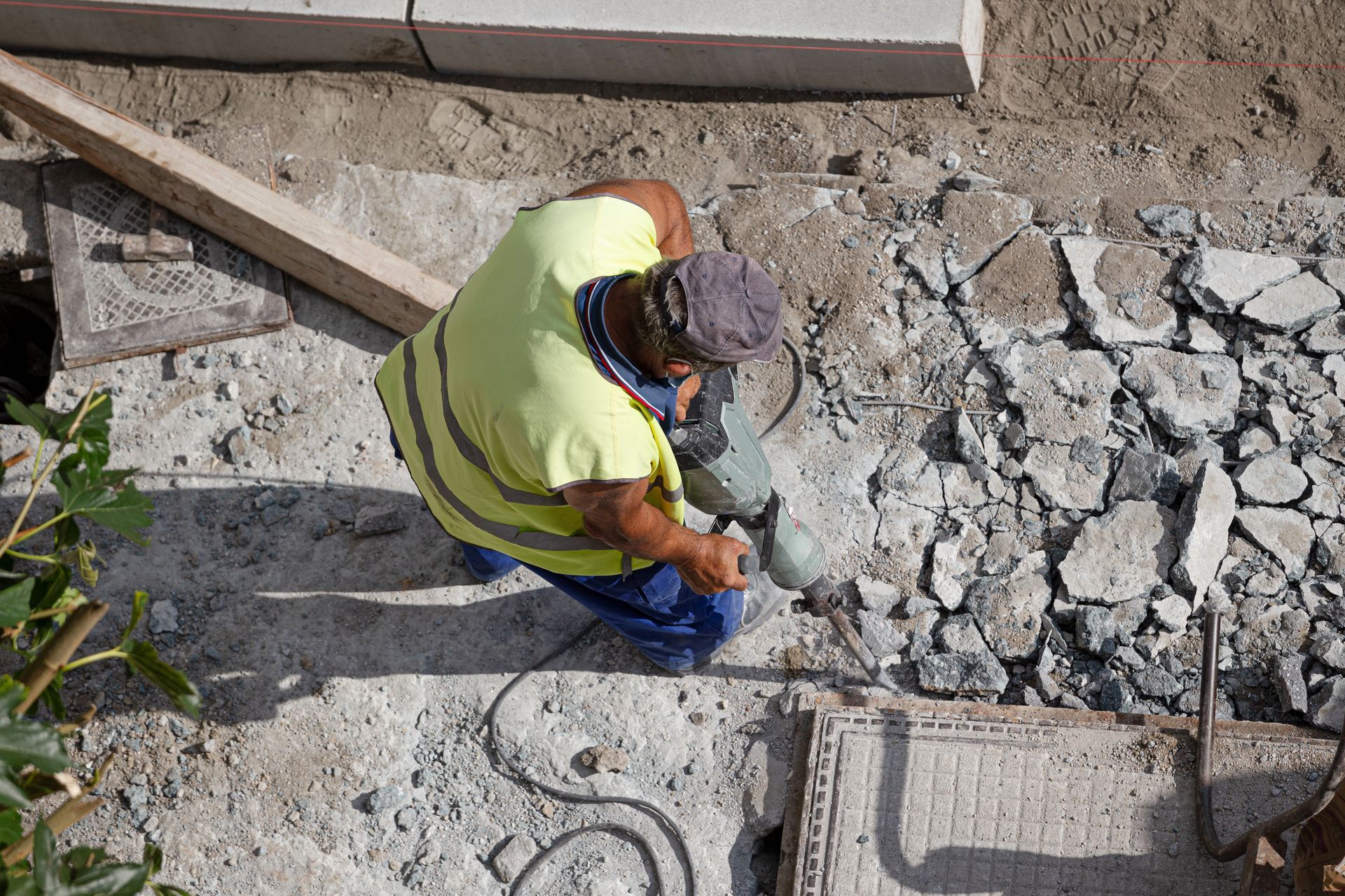 A construction worker is kneeling down on the ground using a hammer.