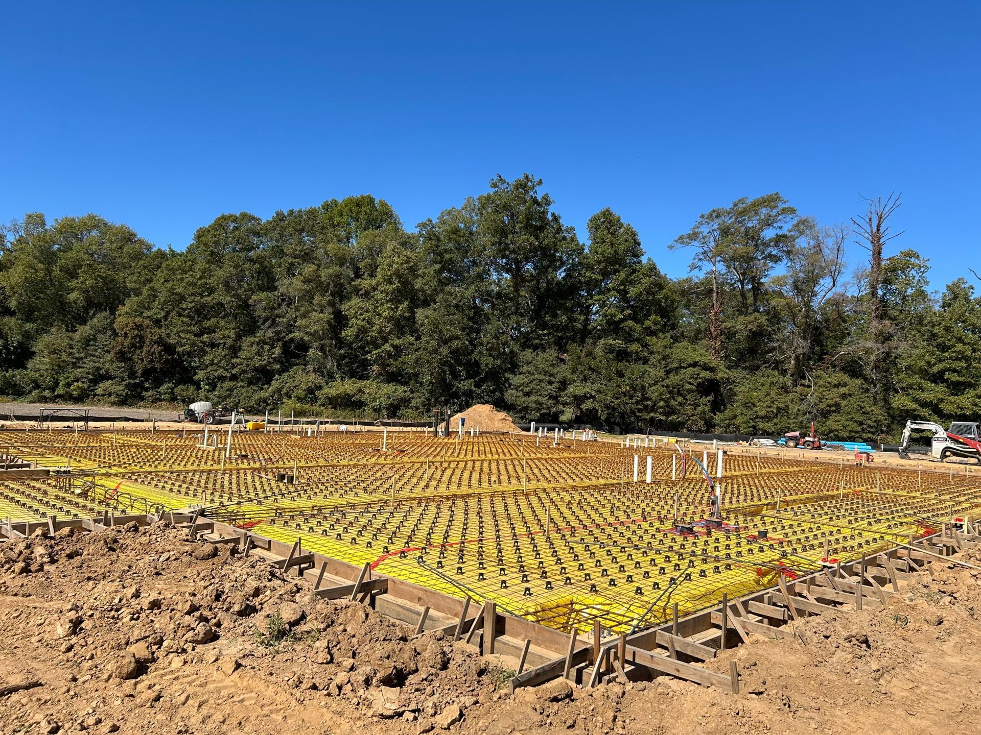 A construction site with a lot of yellow tape on the ground and trees in the background.
