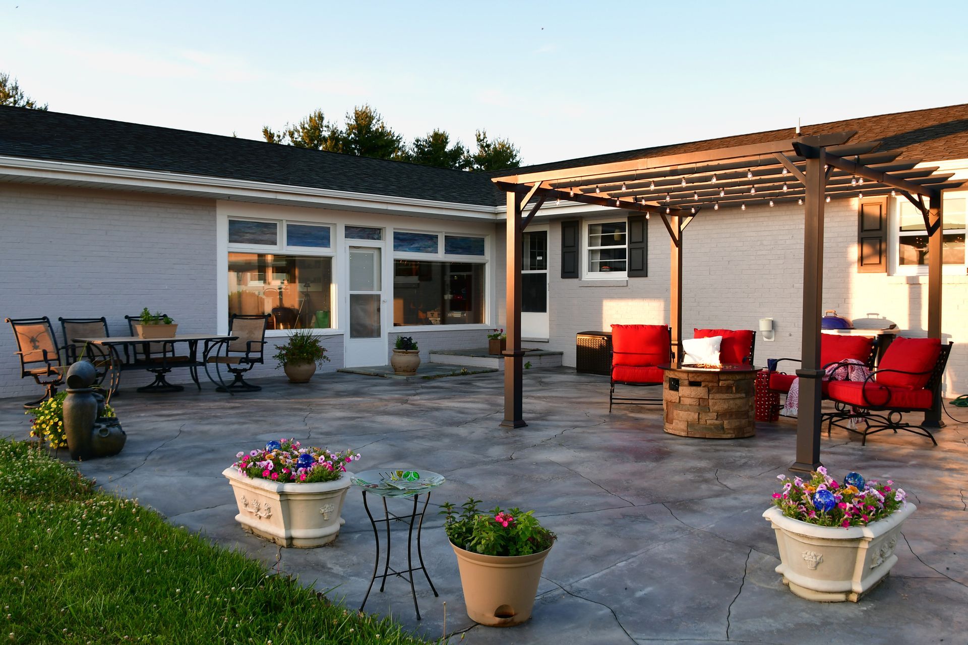 A patio with a pergola and a table and chairs in front of a house.