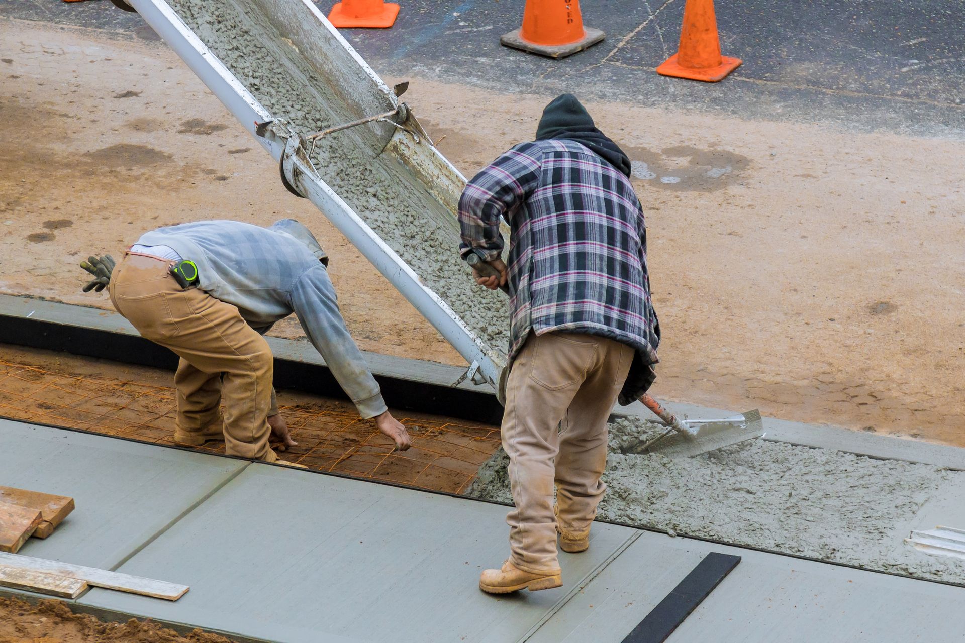 Two men are pouring concrete on a sidewalk.